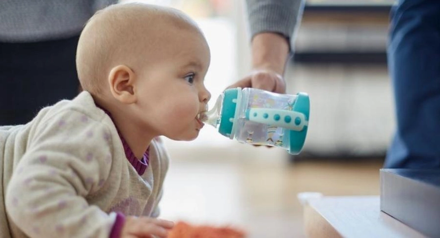 Bé 6 tháng tuổi đang uống nước từ bình